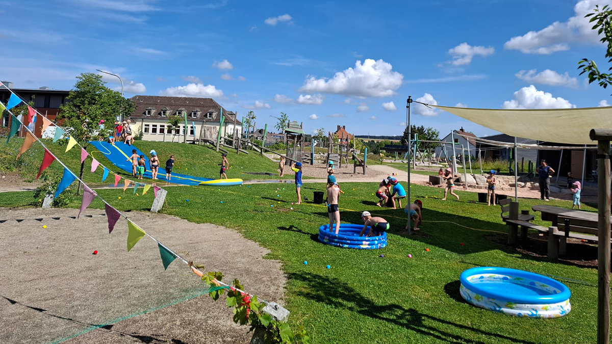 Kinder planschen bei sonnigem Wetter während des LamiKita-Plantschtags in kleinen Pools und rutschen auf einer Wasserrutsche.