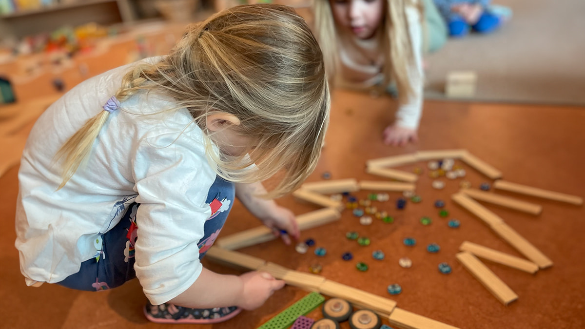 Kinder spielen am Boden mit Holzklötzen und bunten Glassteinen