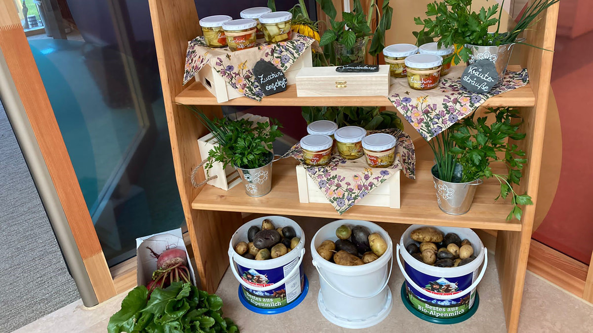  Regal mit Gläsern voller eingelegter Zucchini, frischen Kräutern und Eimern mit Kartoffeln, dekoriert mit Stofftüchern.