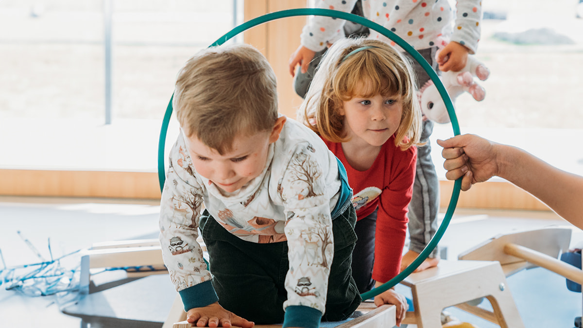 Zwei Kinder krabbeln im Sportraum durch einen Reifen
