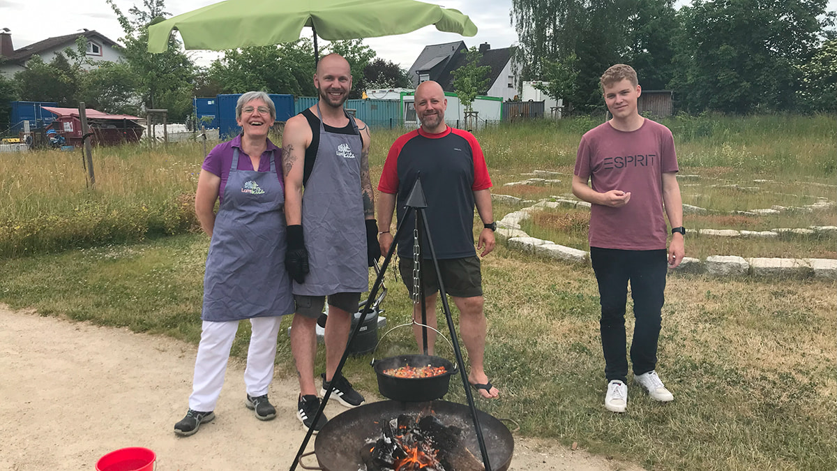 Eltern der LamiKita stehem im Freien um ein Lagerfeuer und kochen mit einem Kessel Eintopf